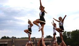 Cheerleaders performing a pyramid stunt on a football field.